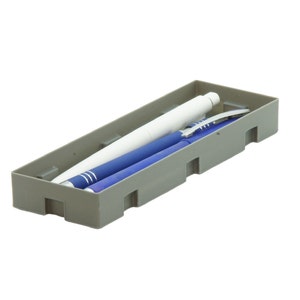 Könnte beinhalten: Ein grauer, rechteckiger Stifthalter mit einem weißen Stift und zwei blauen Stiften. Die Stifte haben unterschiedliche Designs, einer davon mit silbernen Akzenten. Der Halter hat Ausschnitte an den Seiten.