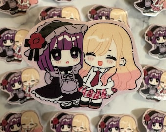 May include: A selection of anime-style stickers depicting two cartoon characters. One character has purple hair and wears a black dress, the other has blonde hair and a school uniform. The stickers are pink and white.