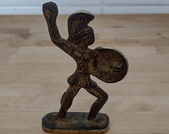 May include: A bronze figurine of a warrior holding a shield, standing on a rectangular base.