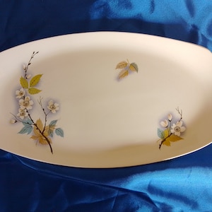 May include: White oval serving platter with a floral design. The design features white flowers, green leaves, and brown branches.