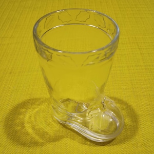 Peut inclure: Un verre à shot en verre transparent en forme de botte. Le verre a un motif décoratif autour du bord.
