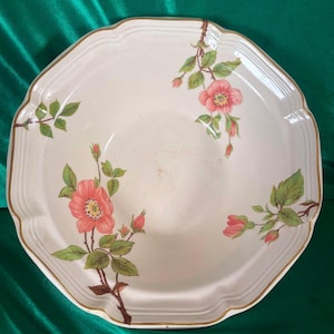 May include: A cream-coloured ceramic bowl with an octagonal rim and a gold-trimmed edge. The interior features a floral pattern of pink wild roses with green leaves and stems, distributed in three distinct clusters around the basin.