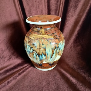 May include: A brown and white ceramic vase with a unique glaze pattern. The vase has a rounded body and a slightly flared opening.