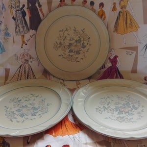 May include: Three white ceramic dinner plates with a blue floral design and a green rim.