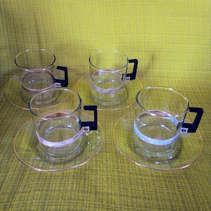 May include: Set of four clear glass cups with black handles and gold trim. Each cup has a matching saucer with a gold rim.