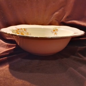 May include: A white ceramic bowl with a pink rim and floral pattern. The bowl has a gold trim around the edge.