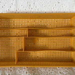 May include: Mustard yellow plastic cutlery tray with multiple compartments. The rectangular tray has a grid pattern throughout and is designed to organise silverware. A practical kitchen storage solution.