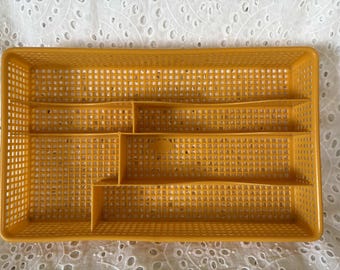 May include: Mustard yellow plastic cutlery tray with multiple compartments. The rectangular tray has a grid pattern throughout and is designed to organize silverware. A practical kitchen storage solution.