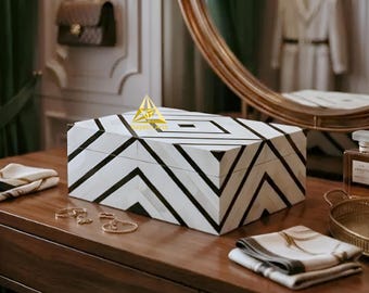May include: A rectangular storage box featuring a white and black geometric chevron pattern across its lid and sides. The box displays a gold-colored triangular logo with the text Gayatri Arts on the top surface, showcasing a clean, structured design.