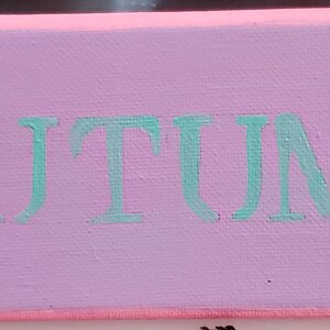 K&ouml;nnte beinhalten: Eine rosa Leinwand mit dem Wort "AUTUMN" in T&uuml;rkis. Zwei schwarze Silhouetten von Meerjungfrauen mit Fl&uuml;geln befinden sich auf beiden Seiten des Wortes.