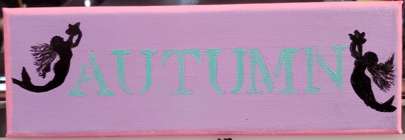 K&ouml;nnte beinhalten: Eine rosa Leinwand mit dem Wort "AUTUMN" in T&uuml;rkis. Zwei schwarze Silhouetten von Meerjungfrauen mit Fl&uuml;geln befinden sich auf beiden Seiten des Wortes.