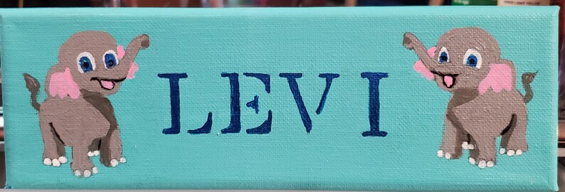 K&ouml;nnte beinhalten: Ein t&uuml;rkisfarbenes Leinwand-Schild mit zwei grauen Elefanten mit rosa Ohren und wei&szlig;en Akzenten. Der Name "LEVI" ist in blauen Buchstaben gemalt.