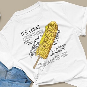 Può includere: Maglietta bianca con una grafica di una pannocchia di mais e il testo "It's corn! A big lump with knobs and the juice. I can't imagine a more beautiful thing. I mean look at this thing!"