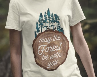Puede incluir: Camiseta blanca con un diseño circular de veta de madera que presenta una escena de bosque y el texto "que el bosque esté contigo".