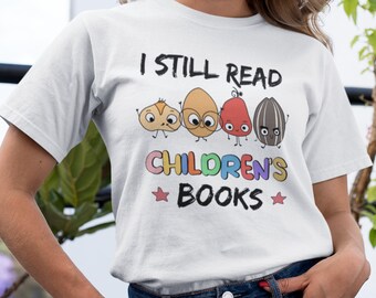 May include: White t-shirt with the text "I still read children's books" in black. The text is surrounded by four cartoon characters that look like nuts and seeds.