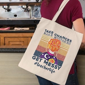 Op de afbeelding: Een witte tote bag met een retro-ontwerp met een vrouw met een bloem op haar hoofd. De tekst op de tas luidt "Take Chances Make Mistakes Get Messy #teacherlife".
