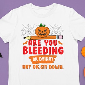 Op de afbeelding: Wit T-shirt met een afbeelding van een jack-o'-lantern op een potlood met spinnenwebben. De tekst luidt "Are you bleeding or dying? No? Ok, sit down."