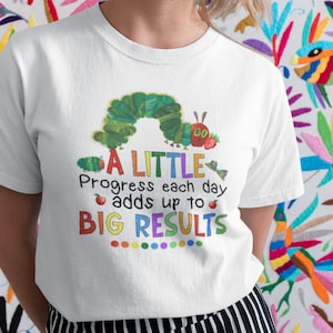 May include: White t-shirt with a colorful graphic of a caterpillar and the text "A LITTLE Progress each day adds up to BIG RESULTS".