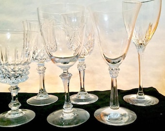 May include: A set of six clear glass wine glasses with different styles and designs. The glasses are arranged in a row on a black surface.
