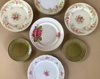 May include: Set of seven vintage floral and green patterned plates. The plates are various sizes and feature floral designs with pink, white, and green accents.