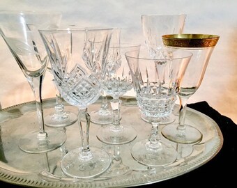 May include: A set of seven clear glass wine glasses with various shapes and designs, including a coupe, a martini glass, and a stemmed wine glass. The glasses are arranged on a silver tray.