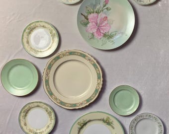 May include: A collection of nine decorative plates with floral and green designs. The plates are arranged in a circular pattern on a white background.