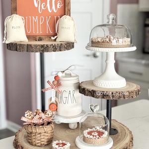 May include: A tiered decorative display featuring a wooden sign that reads "hello PUMPKIN" and two small bags labeled "FLOUR" and "SUGAR". The display includes a glass cloche, a basket, and small decorative cakes, all arranged on wooden slices.