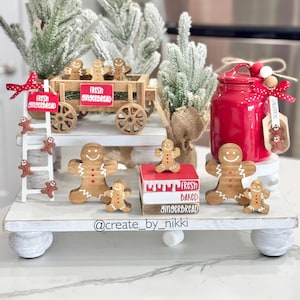 May include: A festive Christmas display featuring gingerbread men, a red jar, and miniature Christmas trees. The display includes a wooden wagon with "Fresh Gingerbread" signs, a ladder, and a tiered stand with decorative elements.