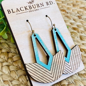 Puede incluir: Pendientes de madera geométricos en azul claro y madera natural. Los pendientes tienen una parte superior geométrica azul claro y una base de semicírculo con un patrón de chevrón. Se muestran en una tarjeta de madera con el texto "BLACKBURN RD. DESIGNS".