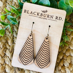 May include: A pair of wooden earrings with a geometric chevron pattern. The earrings are on a wooden display card with the text "Blackburn Rd. Designs".