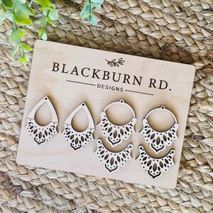 May include: Six unfinished wooden earring blanks with intricate laser-cut designs. The blanks are arranged on a wooden board with the text "Blackburn Rd. Designs" printed on it.
