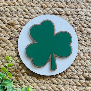Peut inclure: Une découpe de trèfle vert sur un fond rond en bois blanc. Le trèfle est un symbole irlandais traditionnel.