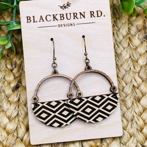 Könnte beinhalten: Hölzerne Ohrringe von Blackburn Rd. Designs mit einem geometrischen Muster in Schwarz und Weiß. Die Ohrringe haben die Form eines Halbkreises mit einem goldfarbenen Haken aus Metall.