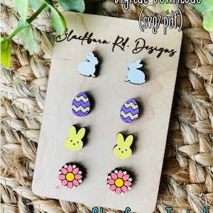 May include: A set of six wooden earrings featuring Easter-themed designs. The earrings include two bunny rabbits, two Easter eggs, and two flowers. The earrings are displayed on a wooden card with the text "Blackburn Rd. Designs" and "Glowforge Tested".