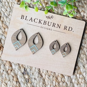 Könnte beinhalten: Drei Holzohrringe mit geometrischen Mustern in Braun, Beige und Weiß. Die Ohrringe werden auf einem Holzbrett mit dem Text "Blackburn Rd. Designs" präsentiert.