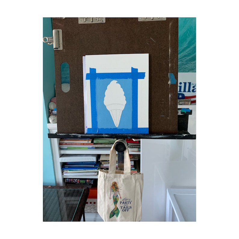 Pu&ograve; includere: Dipinto di un cono gelato in corso, fissato a un cavalletto marrone con nastro adesivo. Una borsa di tela con un'illustrazione di sirena e il testo "Let's Party Tails Off" &egrave; appesa sotto. Lo sfondo include un muro blu e una mensola bianca.