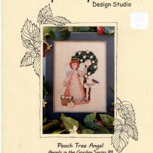 May include: Cross stitch pattern featuring a peach tree angel with a basket of peaches and a bluebird. The pattern is titled "Peach Tree Angel" and is part of the "Angels in the Garden Series #4".