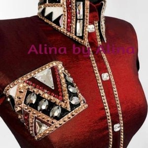 K&ouml;nnte beinhalten: Ein burgunderfarbenes Reitshirt mit einem gold- und schwarzbesetzten Kragen und einer passenden, besetzten &Auml;rmelmanschette. Das Shirt tr&auml;gt den Text "Alina by Alina" auf der Vorderseite.
