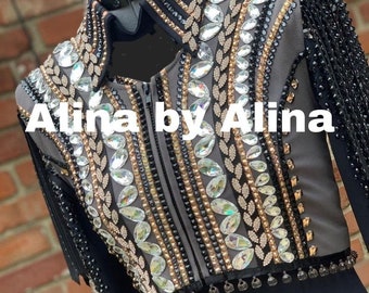 Könnte beinhalten: Eine graue Showjacke mit schwarzen und goldenen Verzierungen, besetzt mit Strasssteinen und Fransen. Die Jacke hat einen Reißverschluss und der Text "Alina by Alina" ist auf der Vorderseite aufgedruckt.
