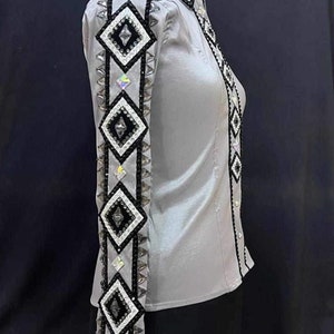 May include: A gray long-sleeve shirt with a black and white geometric design on the sleeves. The design features rhinestones and a diamond pattern.
