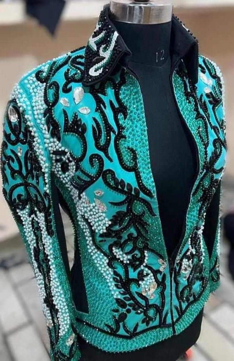 May include: A turquoise and black show jacket with a zipper closure and intricate beading and embroidery. The jacket has a collar and long sleeves.