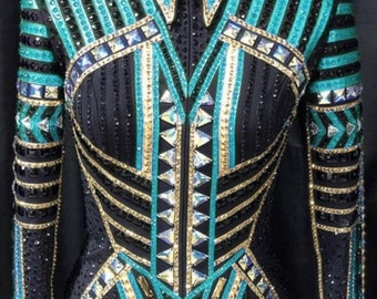 May include: A black show jacket with turquoise and gold trim. The jacket is decorated with rhinestones and has a zipper closure. The text "Alina by Alina" is printed on the front of the jacket.