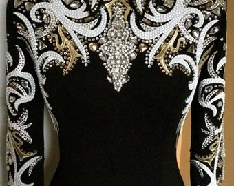 Può includere: Una camicia nera a maniche lunghe con ricami bianchi e dorati e strass. La camicia ha un colletto alto e una silhouette aderente.