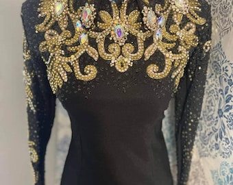 May include: A black long-sleeved shirt with a gold and crystal embellishment on the front. The shirt has a collared neckline.