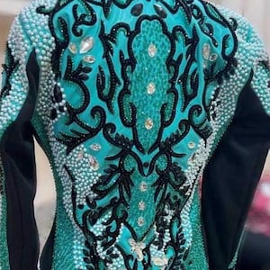 May include: A turquoise and black show jacket with intricate beading and embroidery. The jacket features a floral design with a butterfly in the center.
