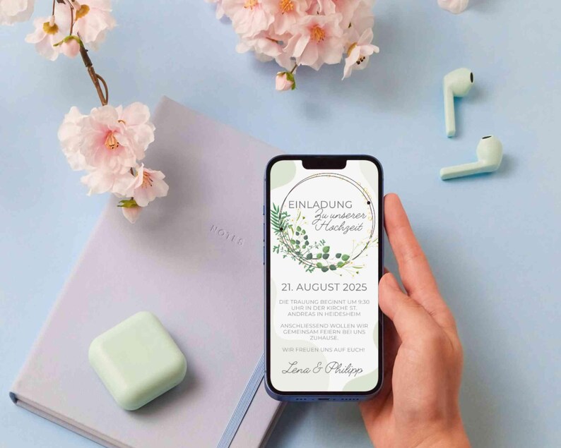 May include: A smartphone displaying a wedding invitation with a green and white floral design. The invitation reads "Einladung zu unserer Hochzeit" and lists the date "21. August 2025".