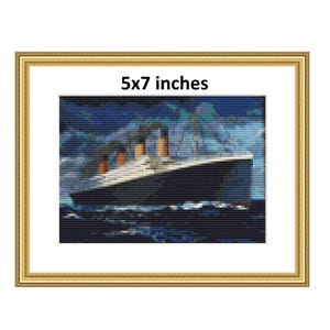Op de afbeelding: Een ingelijst kruissteek van de RMS Titanic die op een donkerblauwe zee vaart. Het schip is wit met oranje reddingsboten en de tekst "5x7 inch" is op de lijst gedrukt.