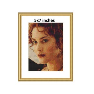 May include: Framed portrait of a woman, 12.7 x 17.8 cm, in a gold frame. The image is a pixelated cross-stitch design. The woman has brown hair and is looking to the side. The text "5x7 inches" is at the top.