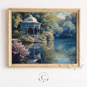 May include: A framed landscape painting depicting a white gazebo situated on the edge of a calm lake, surrounded by lush green trees and pink flowering bushes. The scene features a clear reflection of the gazebo in the water and a light blue sky.