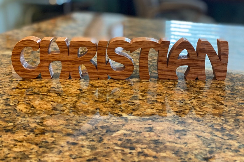 May include: Wooden name sign spelling "Christian" in a decorative font. The letters are made of light brown wood with a natural grain pattern.